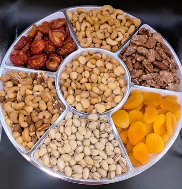 plums, cashews, mixed nuts, pistachios, apricots, macadamia nuts, and praline pecans displayed in a platter